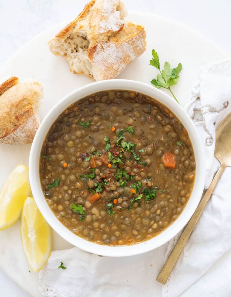 Top view of a white bowl full of green lentil soup served with bread.