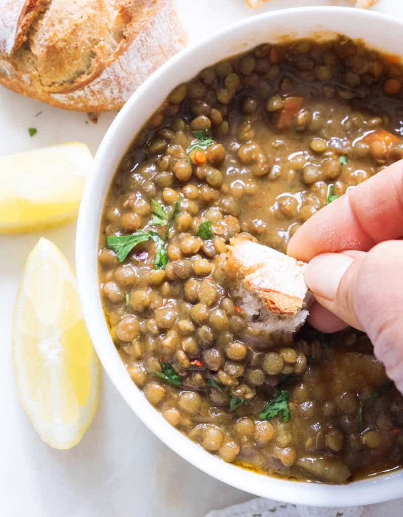 Close-up of a piece of bread dunked into a bowl full of green lentil soup.