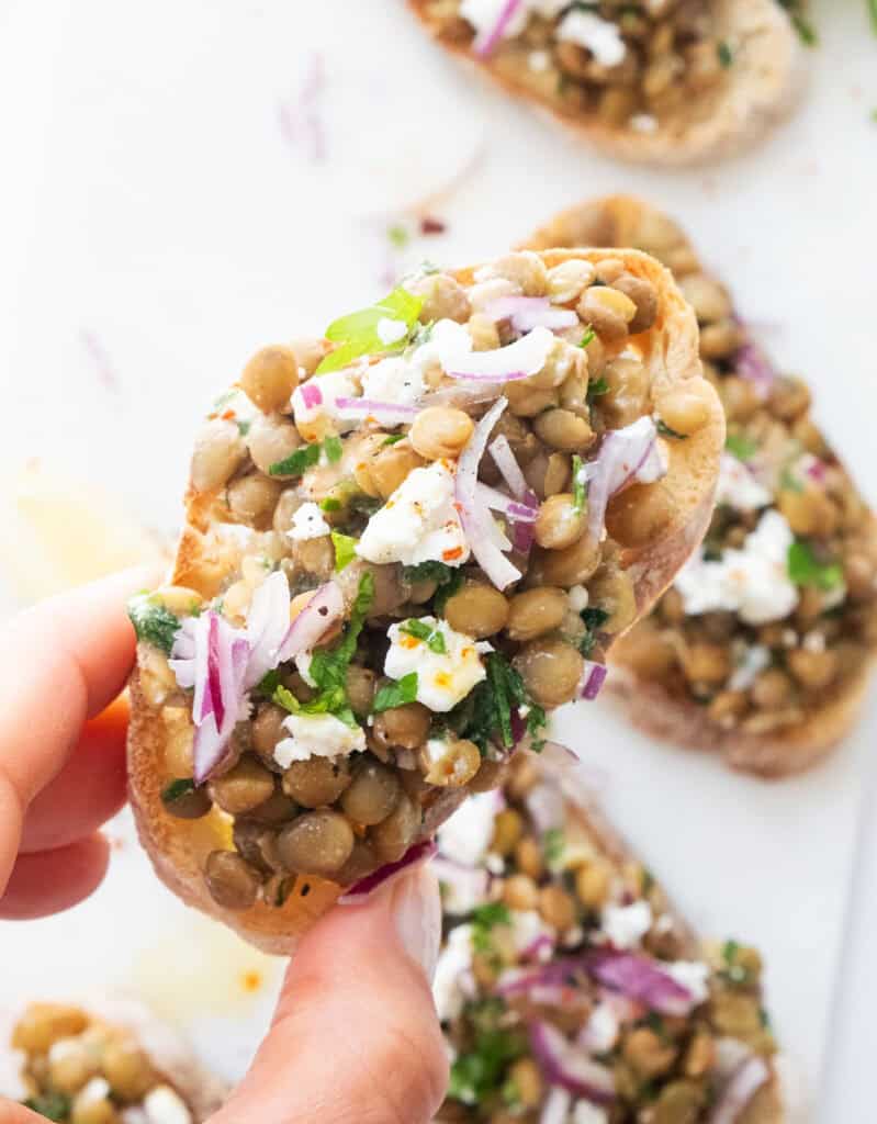 Close-up of a lentil bruschetta topped with feta and red onion.
