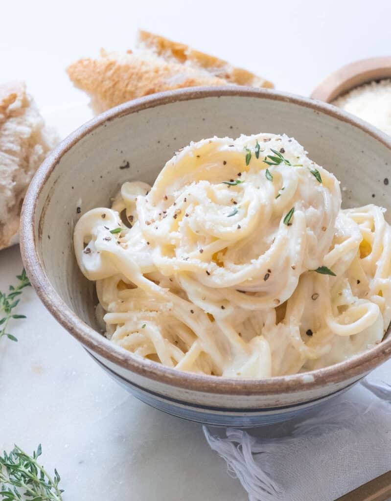 A bowl full of creamy goat cheese pasta over a white background.